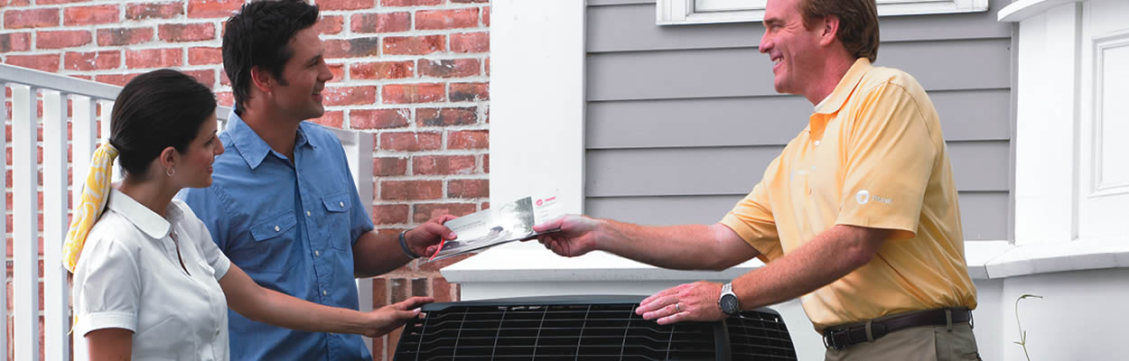 Hvac Tech Handing Brochure To Homeowners While Standing Next To Trane Ac Unit